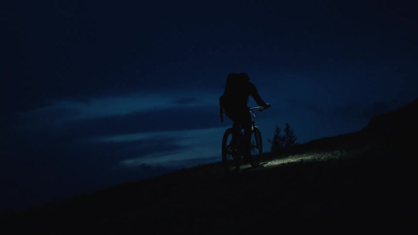 The view is of a man that is riding his bike around the night time