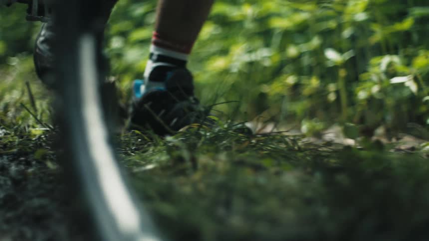 Close up of the feet of a man pushing a mountain bike on a road in the countryside