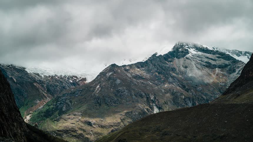 Mountain range with snow and valley under time lapse cloud cover