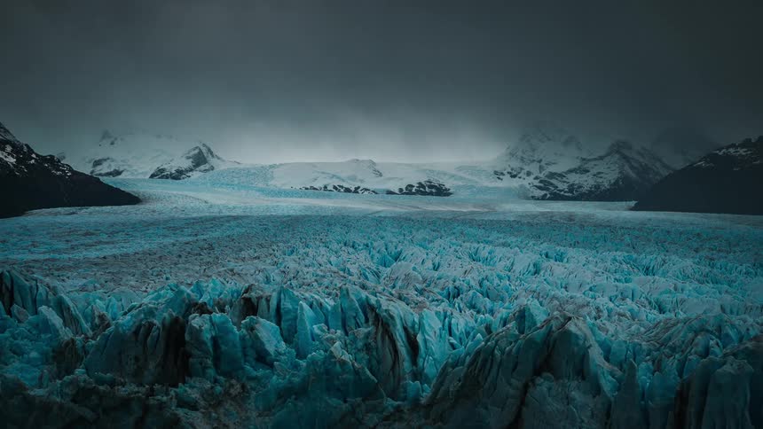 A thick layer of ice and snow covers the ground below a mountain range