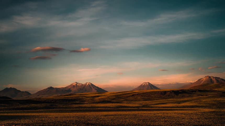 Clouds move across the sky as the sun is setting and there are mountains in the distance