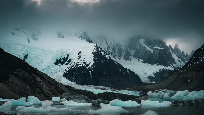 Ice floating on a body of water next to snowy mountains in nature
