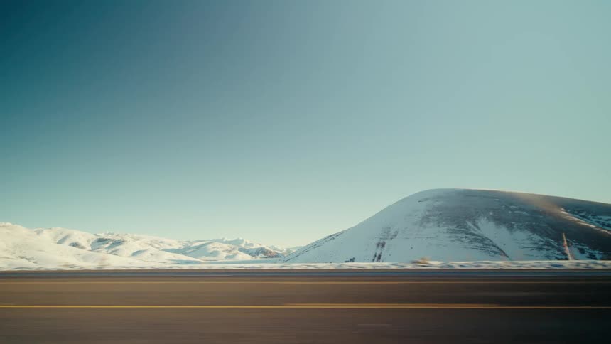 View from car on freeway of landscape passing by mountain range with snow high altitude