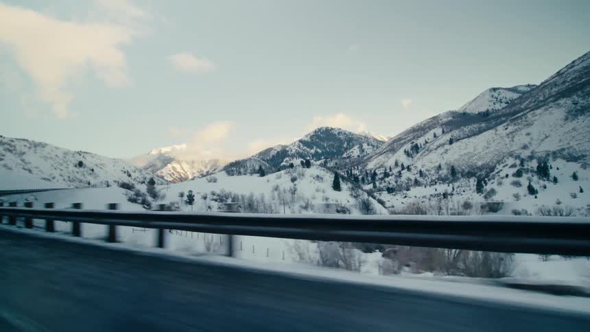 A panoramic view of snowcovered mountains as the camera moves along a highway