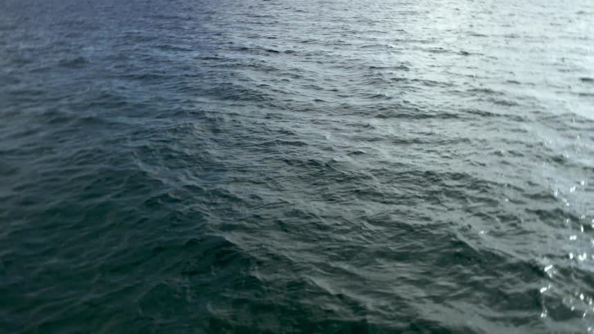 Waves flowing across surface of the ocean gleam while reflecting sunlight