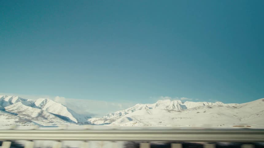 Vehicle drives on highway near highway guardrail snowy field and mountains