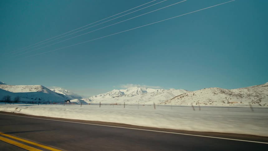 Vehicle drives on highway near the snowy field and mountain ranges
