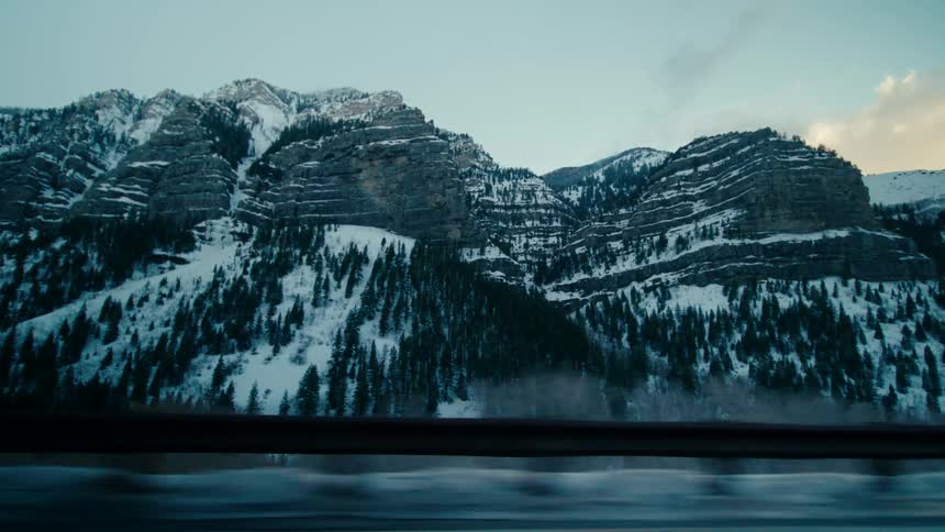 Vehicle drives on highway next to snowy mountains