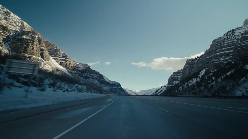 A vehicle drives down a highway past snow capped mountains