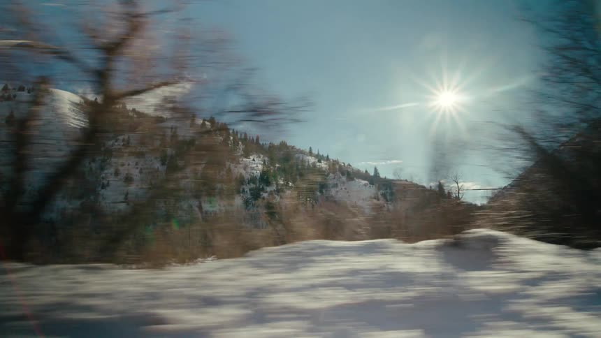 Vehicle drives on highway next to snowy forest and mountain