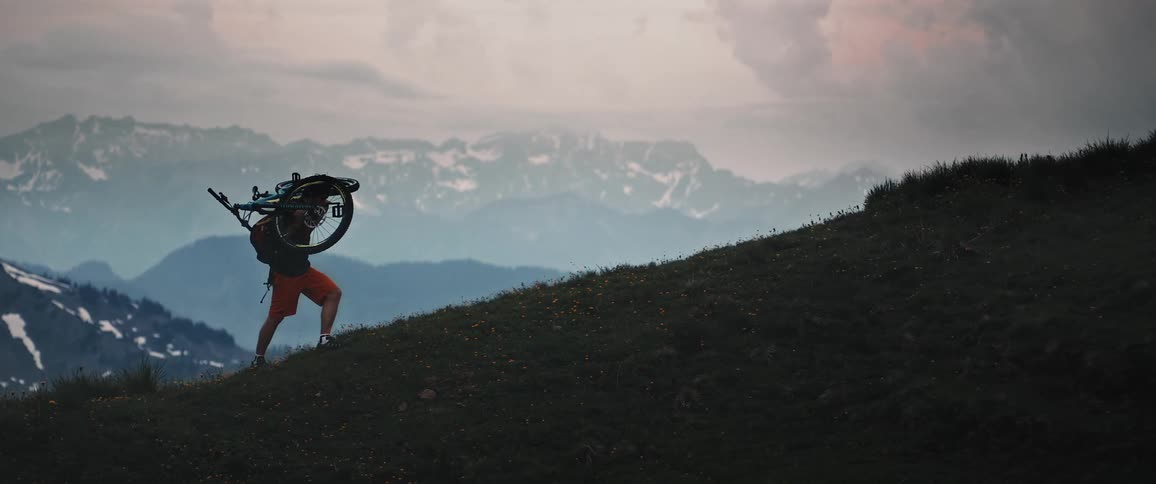 A man carrying a mountain bike up a hillside in nature