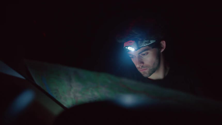 A man is standing outdoors during the night and looking at a map