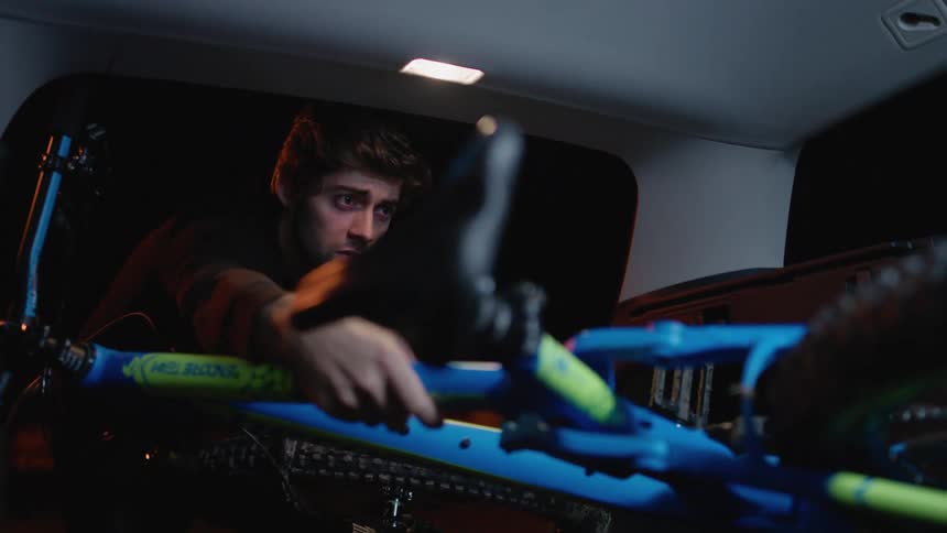 Young man pulls a mountain bike from the trunk of a car at night
