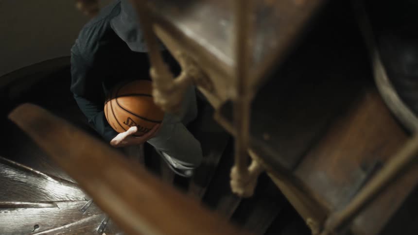 A person with their hood over their head carrying a basketball while walking down stairs