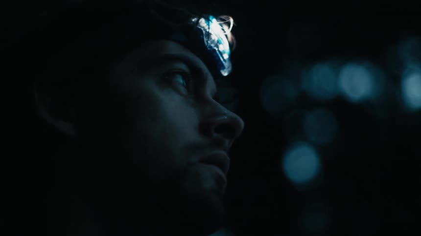 A man is standing outdoors and wearing a flashlight on his helmet