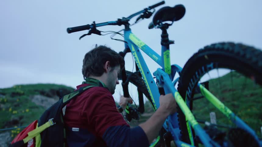 Man going up hiking trail on a mountain picks up mountain bike and carries over his shoulders