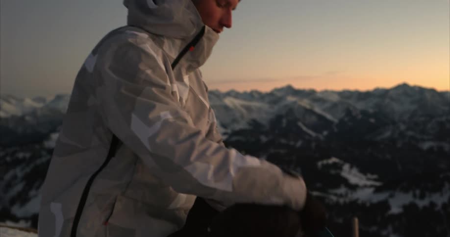 Man puts down backpack on spot overlooking snowy mountains and takes out camera