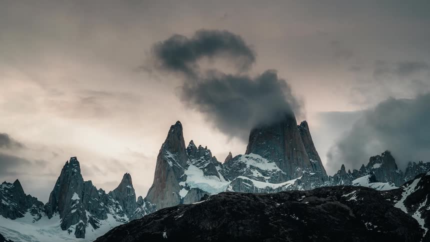 Clouds move over rough mountain peaks with snow along the mountain side