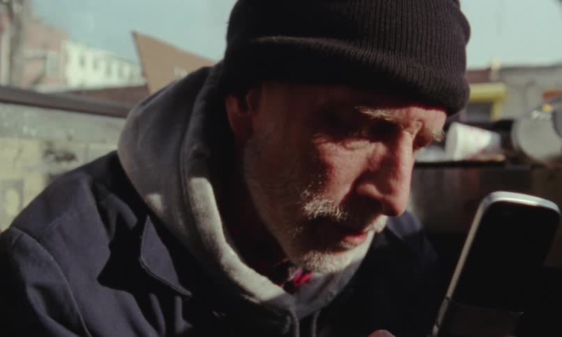 Man in alley near trash filled dumpster tears up after ending phone call