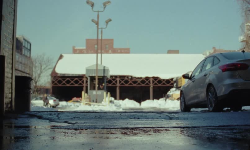 A person is filmed from very far away getting out of their car and walking towards a building
