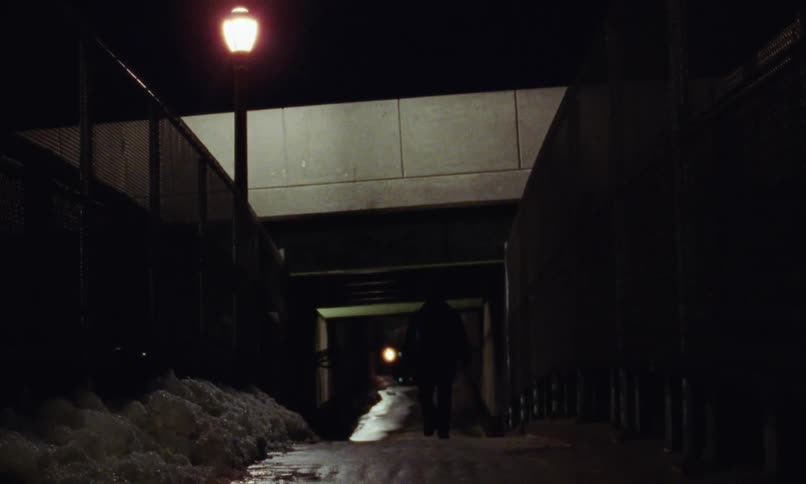 Person walks under bridge on path bordered by walls and snow at night