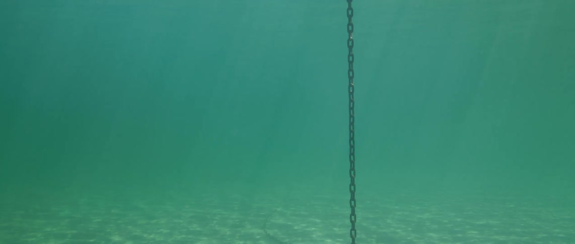 Sunlight shines on the water as a heavy chain from a buoy reaches the seabed
