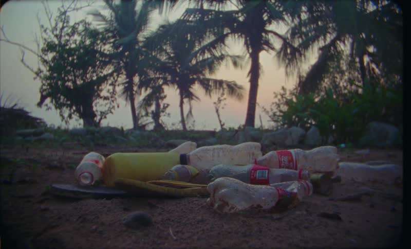 A close up of used bottles and sandals in piles of garbage on the beach