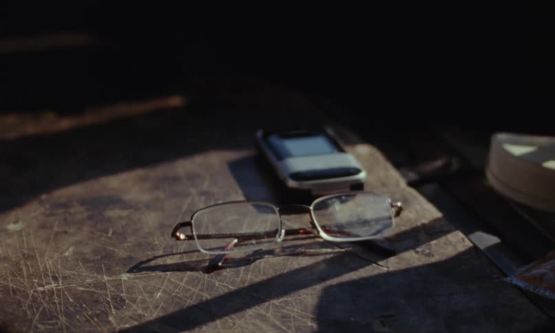 Person wearing fingerless gloves places eyeglasses and other items on scratched wooden surface