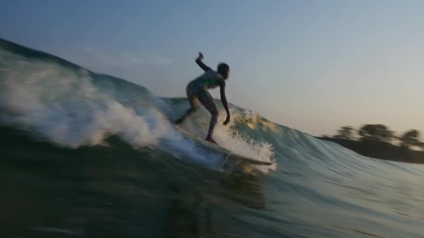 A boy surfs toward the shore at sunset on a wave that submerges the camera