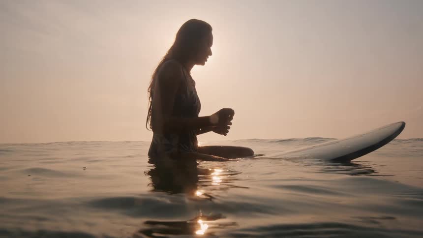 A woman on a surfboard sitting in the ocean