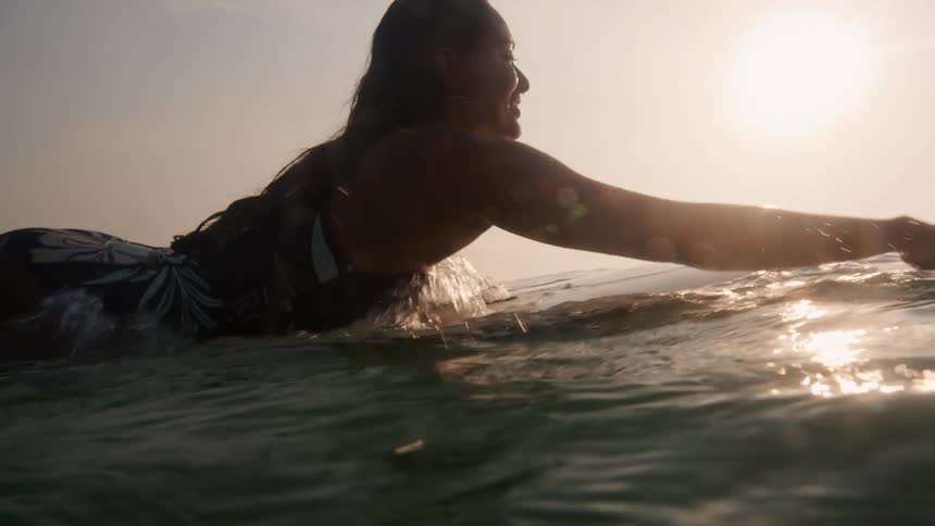 A female is surfing in the ocean at dusk