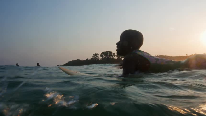 Kids swimming in the sea at sunset or sunrise paddling out on surfboards