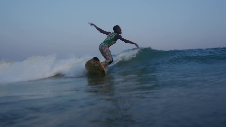 A woman is surfing on a sea wave at dusk