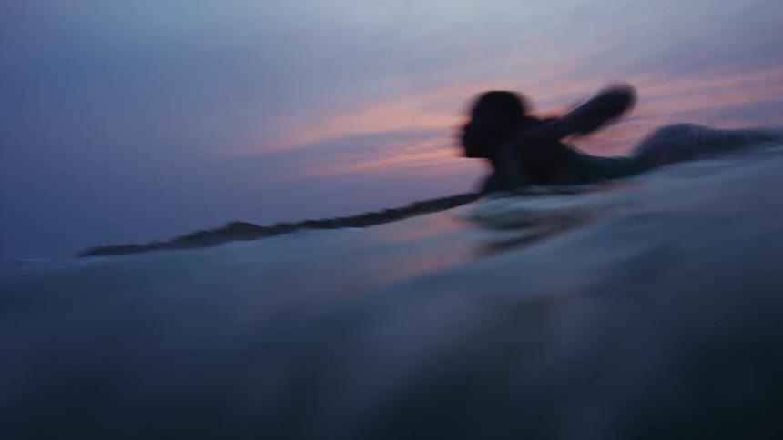A boy is surfing on ocean water at sunset