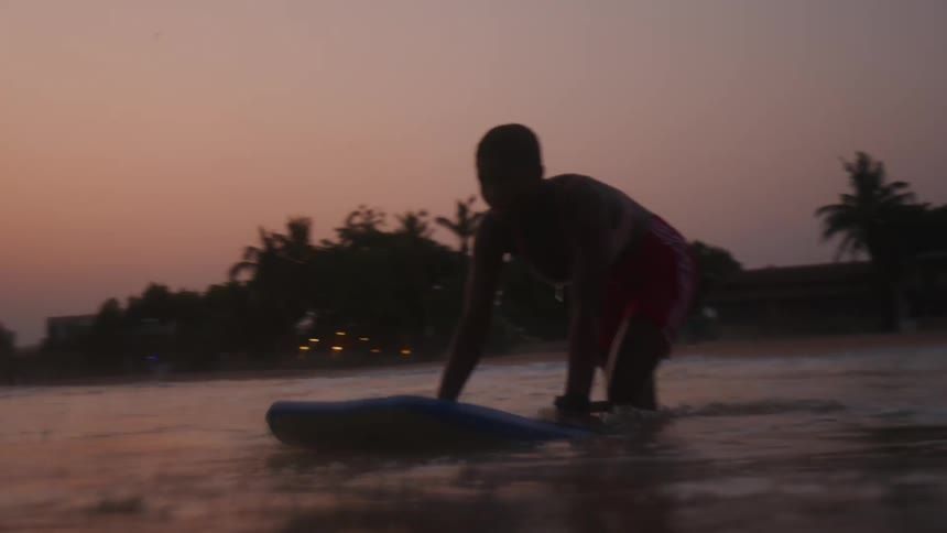 A female is surfing on a body of water at dusk