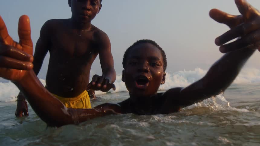 A group of young black boys swim and play in the ocean before a wave midday