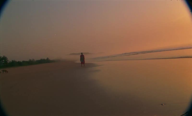 A person is walking on the beach while the sun is setting