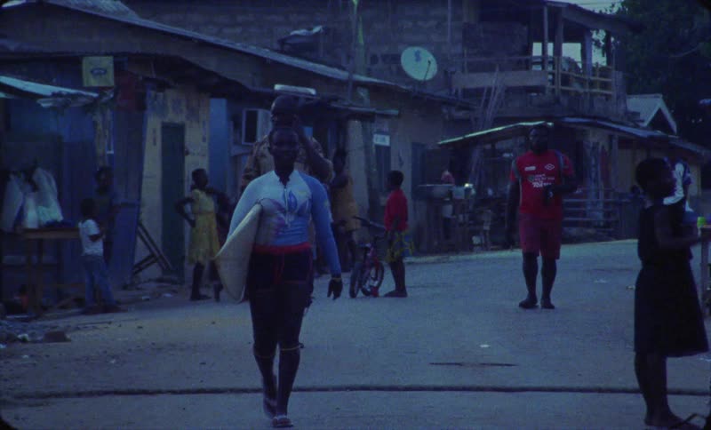 Woman carrying a surfboard walks along busy street