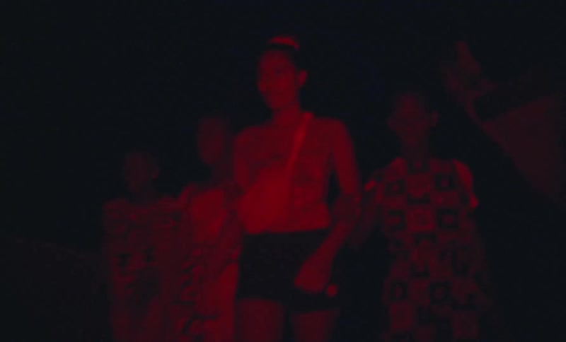 Group of young women walking outdoors at night under red lights caught on vintage film