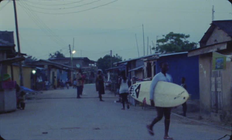 A small crowd walks and stands along an alley of homes and businesses