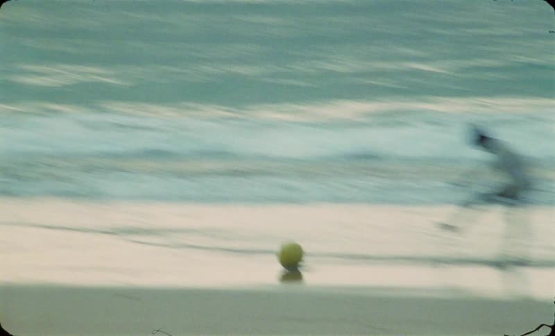 A group of young black boys kick a soccer ball around on an empty beach at dusk