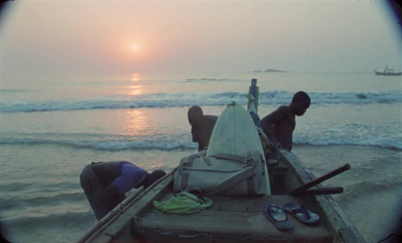 Three teenage boys standing at the shore with a boat and surfboards getting ready for a surfing trip at dawn