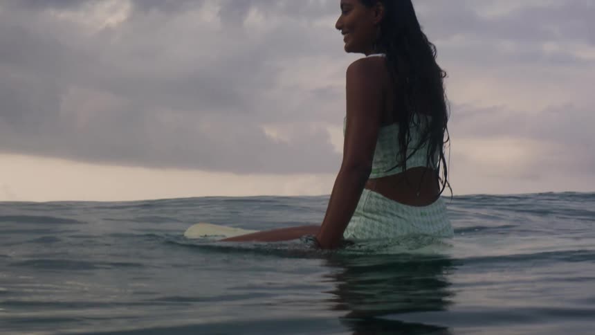 A female is sitting on a surfboard on ocean water