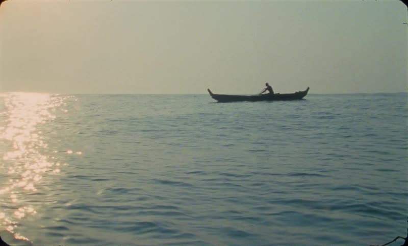 A man is sitting in a boat holding rope and he grabs an oar as he starts rowing across the water