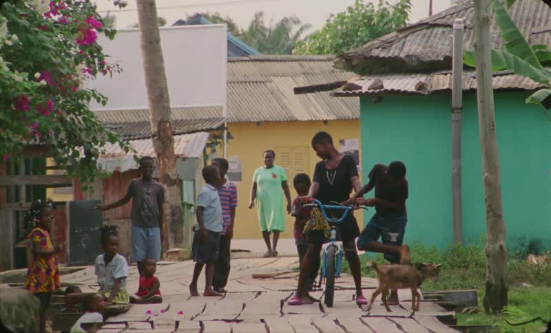 Goat crosses walkway where kids are gathering to talk and look at girls bicycle