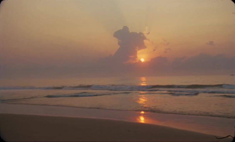 The sun rises or falls behind a cloud over an ocean shoreline