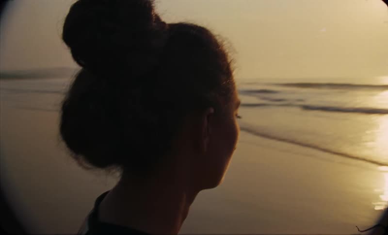 A close up of a womans face as she stares out over the sun setting on the ocean