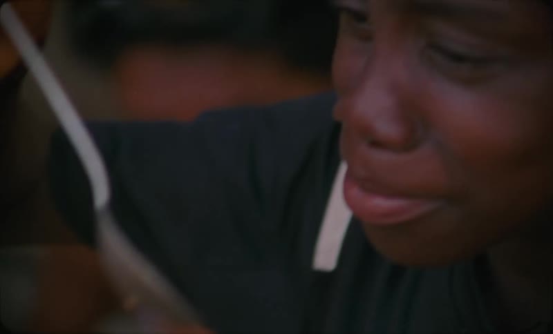 A woman tastes food with a spoon while a woman next to her stirs something in a large bowl