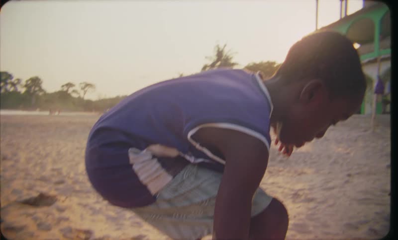A young boy is playing on the beach as he stands on a teetering board trying to keep his balance