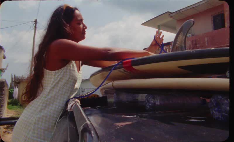 A woman ties a surfboard onto the top of her car